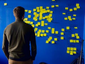 A person in a green sweater looking at a blue wall with yellow sticky notes
